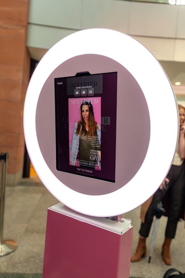 Ring-light iPad photo booth showing a branded magazine-cover photo on its sharing screen at a retail event