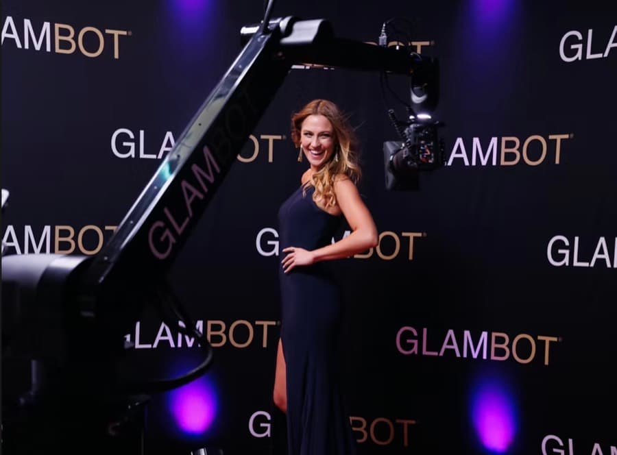 Guest in a floor-length gown posing for a Glambot robot arm camera against a branded backdrop